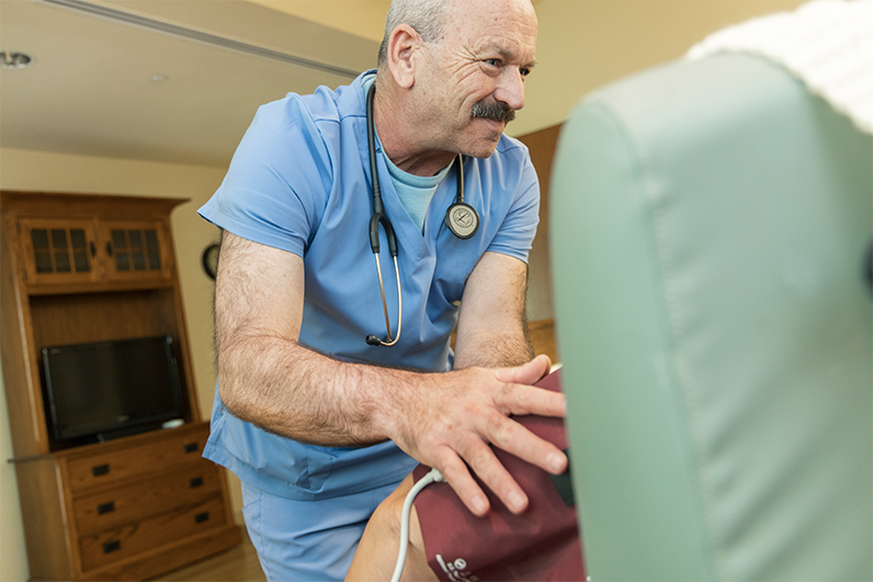 A nurse with a stethoscope around his neck looks down at a sitting patient.